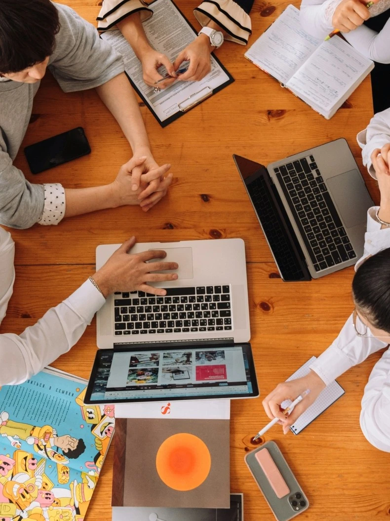 a group meeting, 4 four persons sit by a table with their computer and phone, discuss something with products